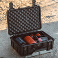 Load image into Gallery viewer, Black hard-shell protective case with egg-crate foam interior holding colorful spray paint cans on sandy ground.