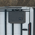 Load image into Gallery viewer, Black rugged hard-shell protective case with reinforced corners and secure latches mounted on vehicle roof rack.
