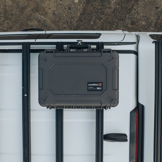 Black rugged hard-shell protective case with reinforced corners and secure latches mounted on vehicle roof rack.