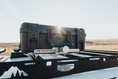 Load image into Gallery viewer, Black hard shell carrying case with secure latches and a label, mounted on a black metal rack against a blurred sky.
