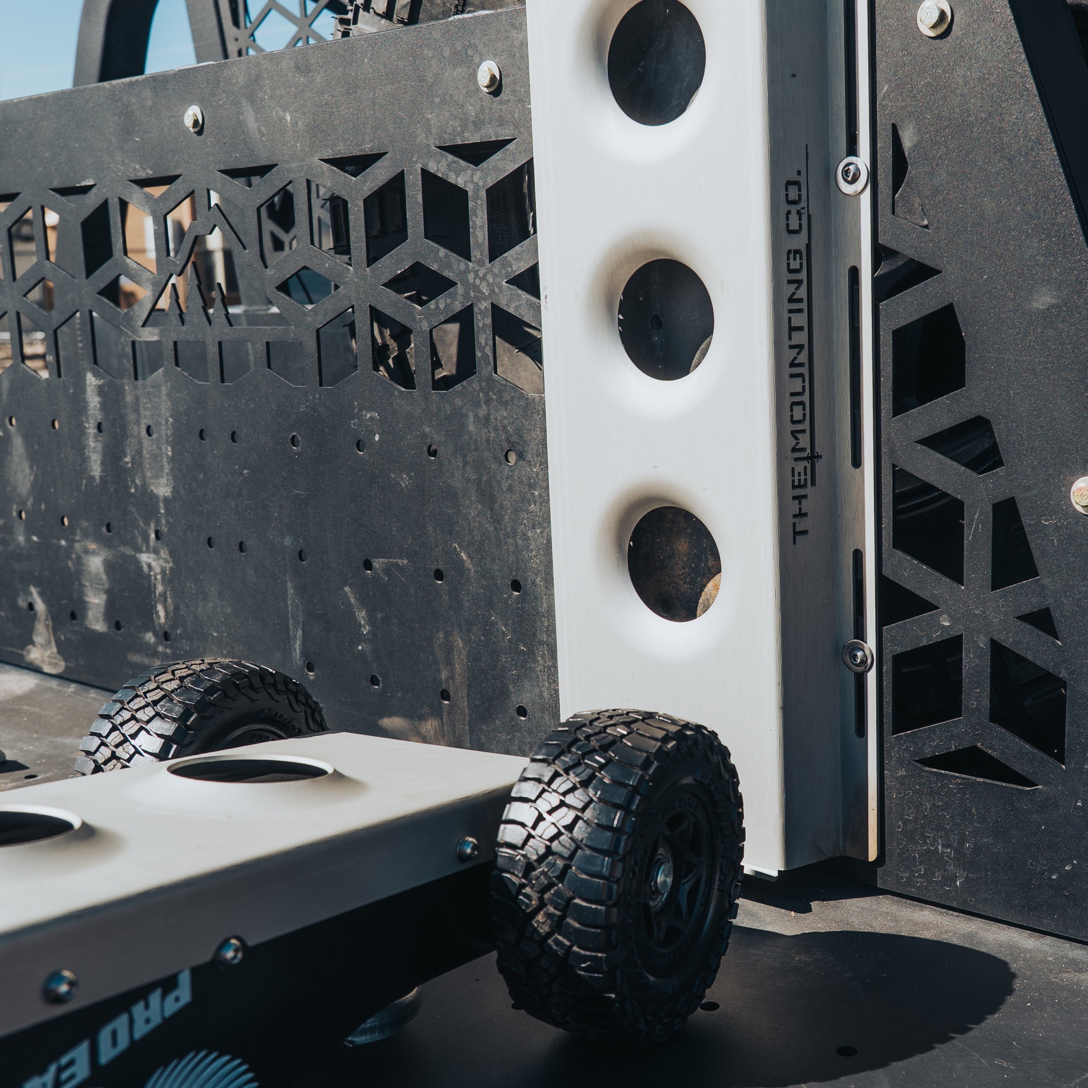 Black heavy-duty jack with textured grip and thick off-road tire against patterned metal backdrop.