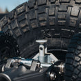 Load image into Gallery viewer, Silver metal jack mount attached near rugged off-road tire with deep tread pattern.
