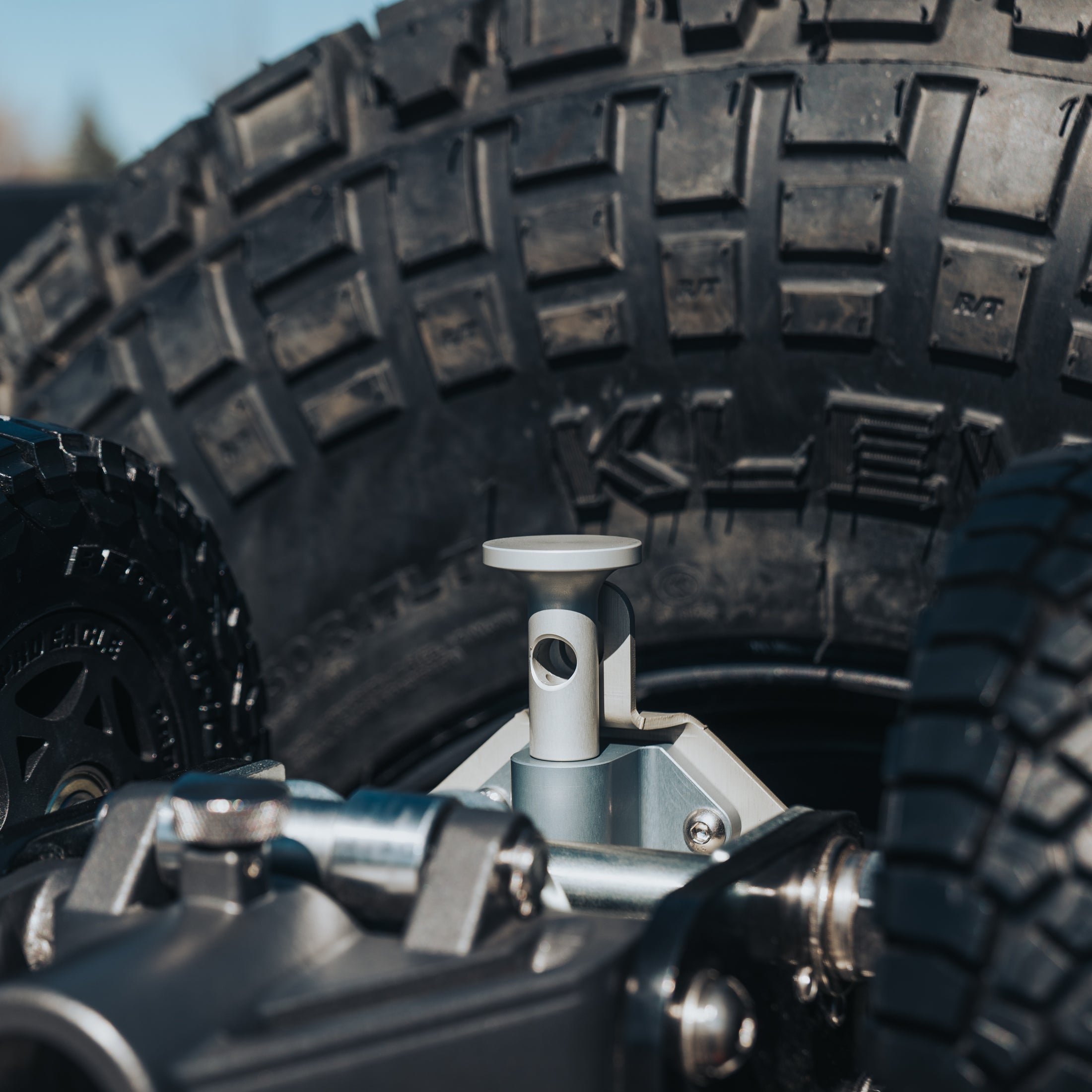 Silver metal jack mount attached near rugged off-road tire with deep tread pattern.
