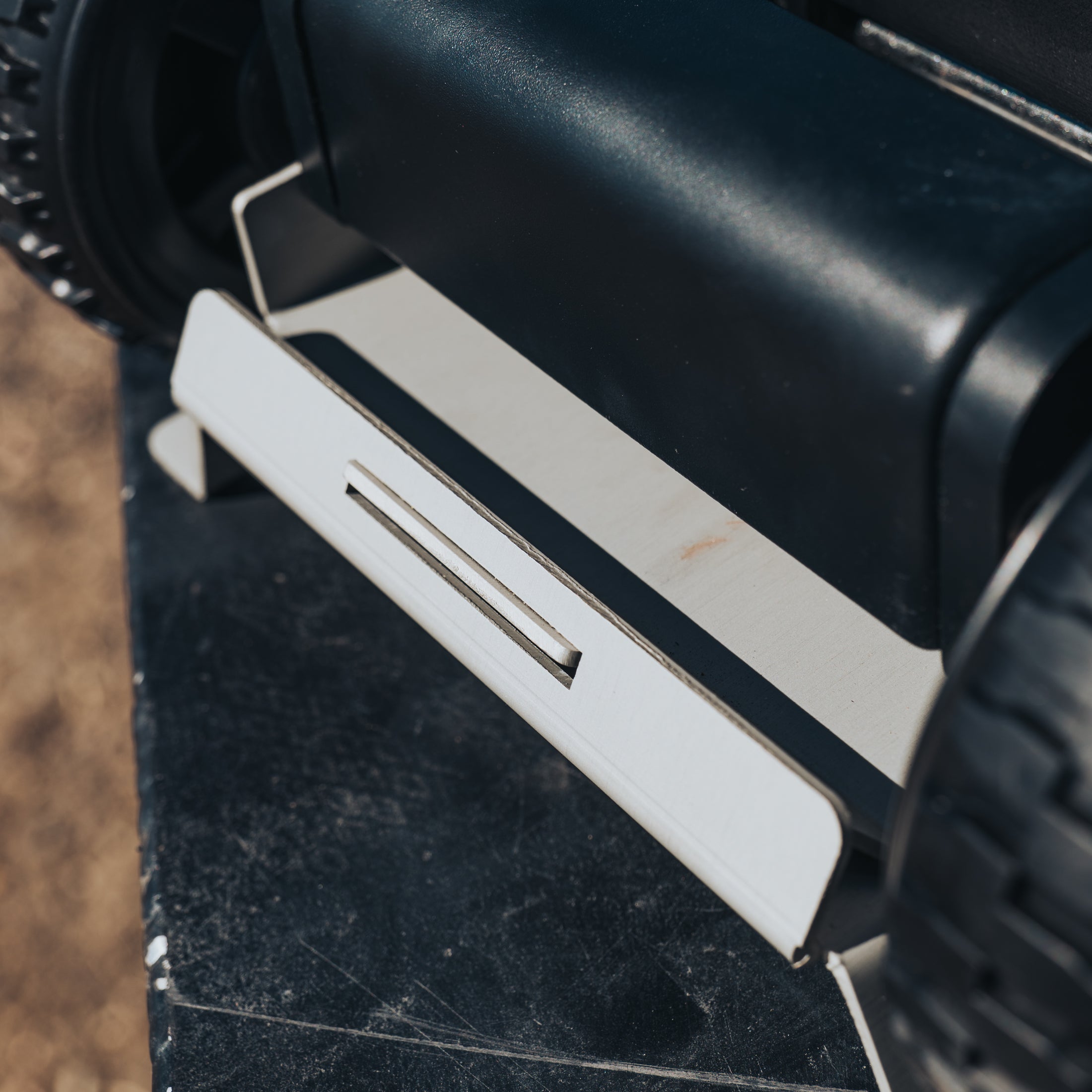 White metal jack mount attached to black rugged vehicle frame with textured surface and large off-road tires visible.