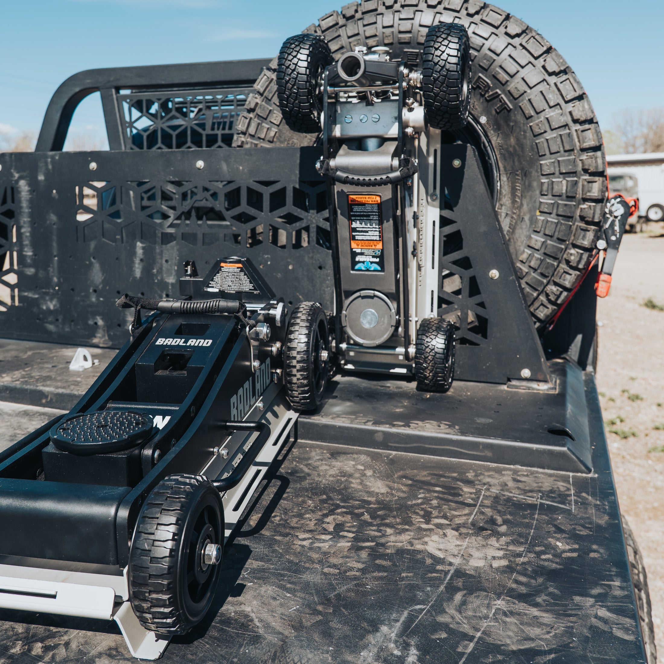 Black 3-ton Badlands Pro Eagle jack with rugged wheels mounted on truck bed, spare tire in background.