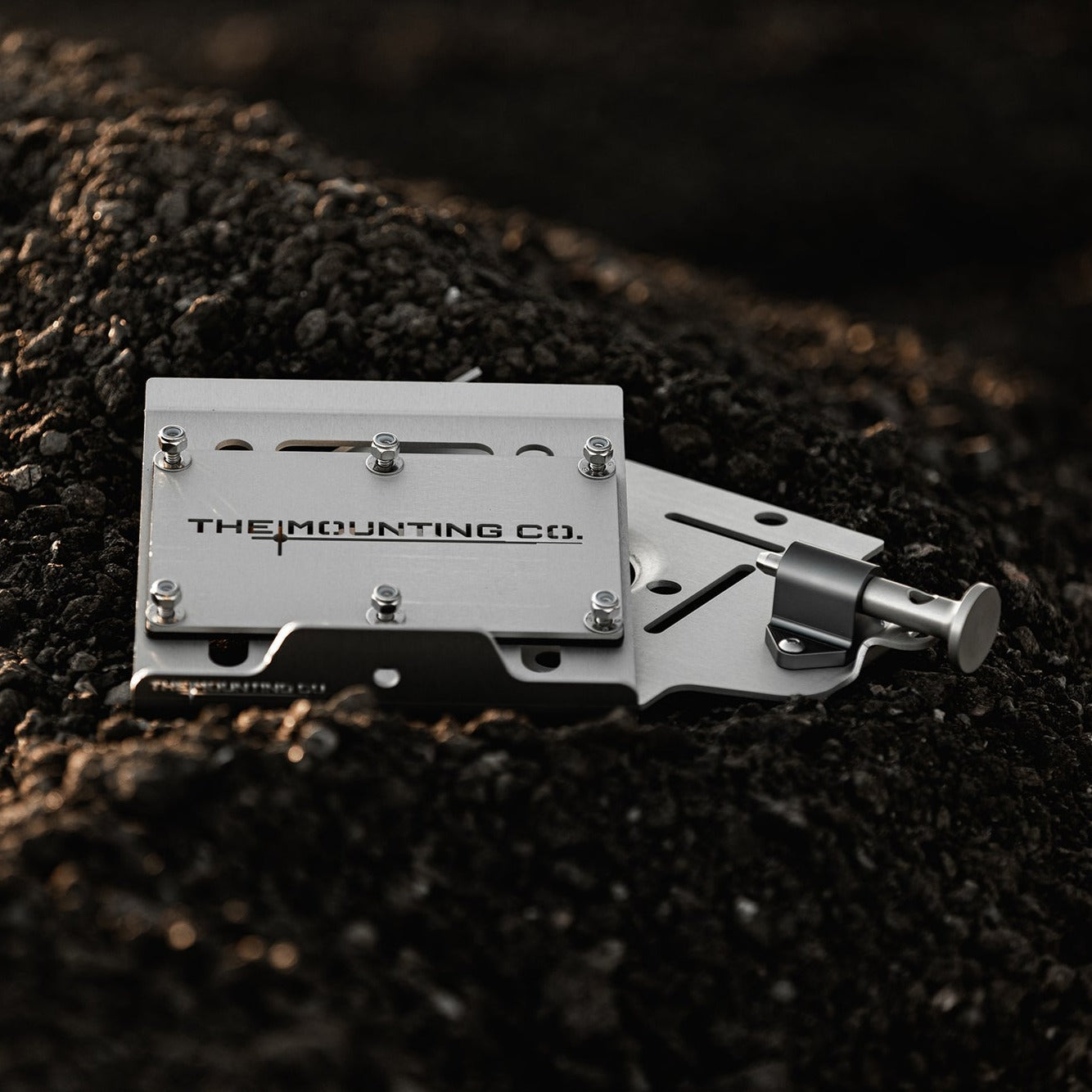 Black aluminum medium quick-release mount with engraved logo and adjustable locking pin on dark soil surface.